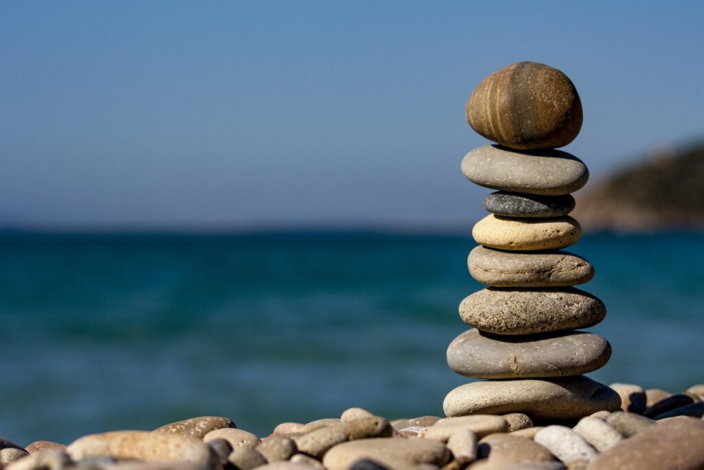 A pile of different sized rocks are balanced in a pile on a rocky beach. 